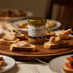 Bloc de foie gras halal Domaine du Périé en pot au centre, entouré de toasts garnis sur plateau en bois lors d’un repas festive.