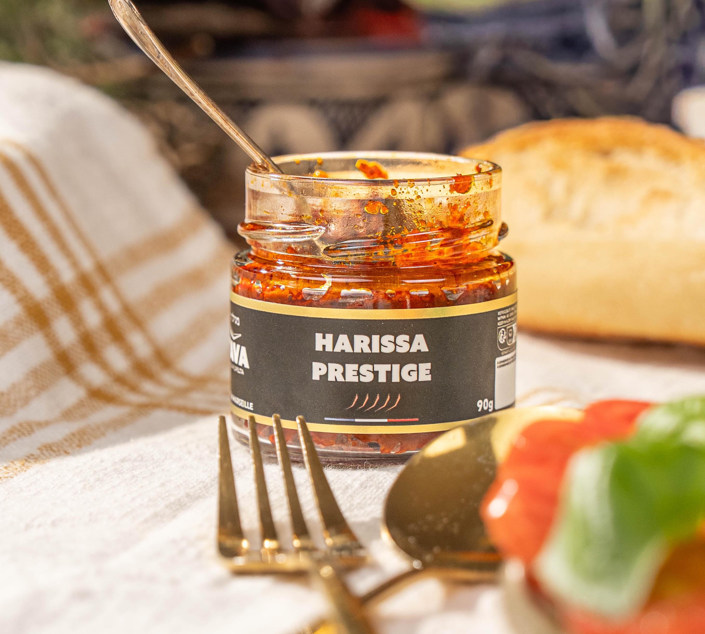 Pot ouvert de harissa prestige Tava Hada Pilpelta avec une cuillère, du pain et des couverts